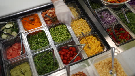 worker assembles colorful salad at vegetable station in restaurant, slow motion slider 4k