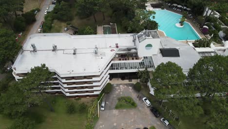 aerial rotating view revealing spacious luxury hotel nestled among verdant pine forest, featuring expansive swimming pool and modern architectural design