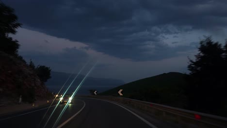 carretera de montaña sobre el pueblo de lin en albania al crepúsculo con cielo oscuro nublado, tráfico conduciendo en la atracción turística del lago de ohrid