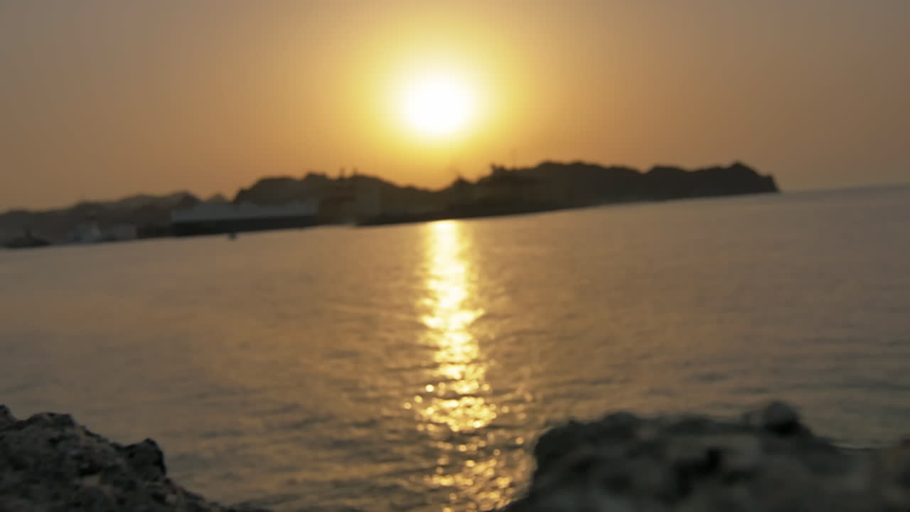 Golden sunset light reflecting across gentle ocean waves with silhouette of port structures