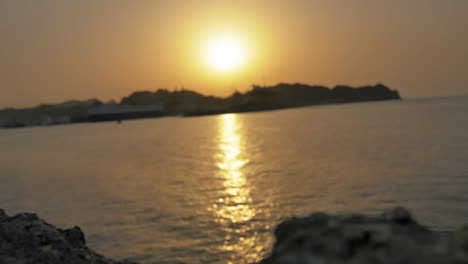 golden sunset light reflecting across gentle ocean waves with silhouette of port structures