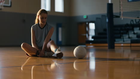 a young athlete sits on a volleyball court with a ball in the foreground