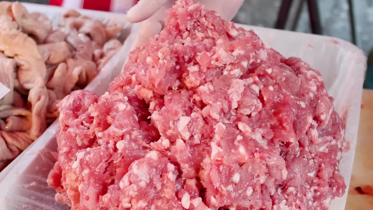 Close-up of gloved hands carefully shaping and handling fresh ground meat on a tray.