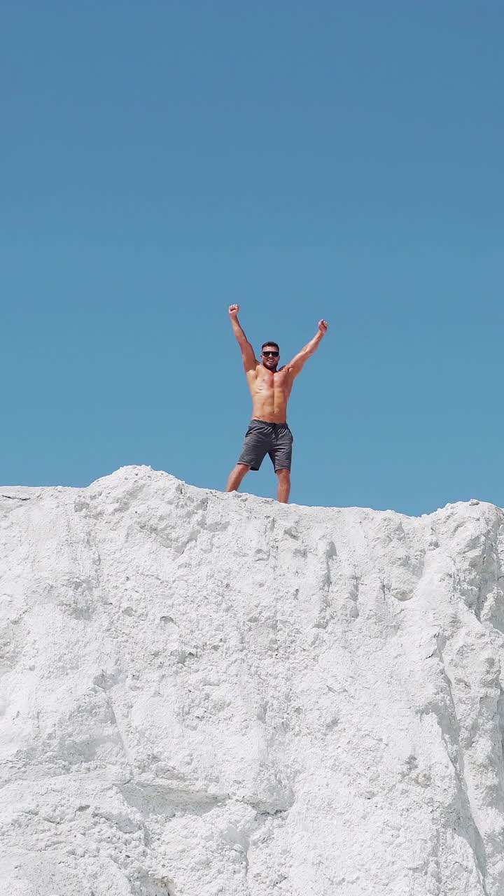 The athlete joyfully celebrates the victory with his hands up. Running athlete on top of the mountain. Vertical video