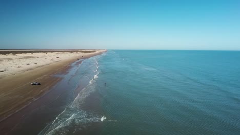 aerial drone view of fisherman standing in surf on beach at low tide on a gulf coast barrier island on a sunny afternoon - south padre island, texas