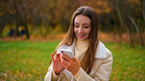 attractive long-haired caucasian lady writing message on the phone. woman using gadget walking in the beautiful autumn park.