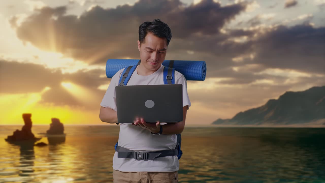 Aziatische mannelijke wandelaar met bergbeklimmersrugzak die een laptop gebruikt op het strand