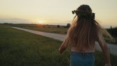 vista trasera de una niña caucásica corriendo hacia la puesta de sol en el prado.