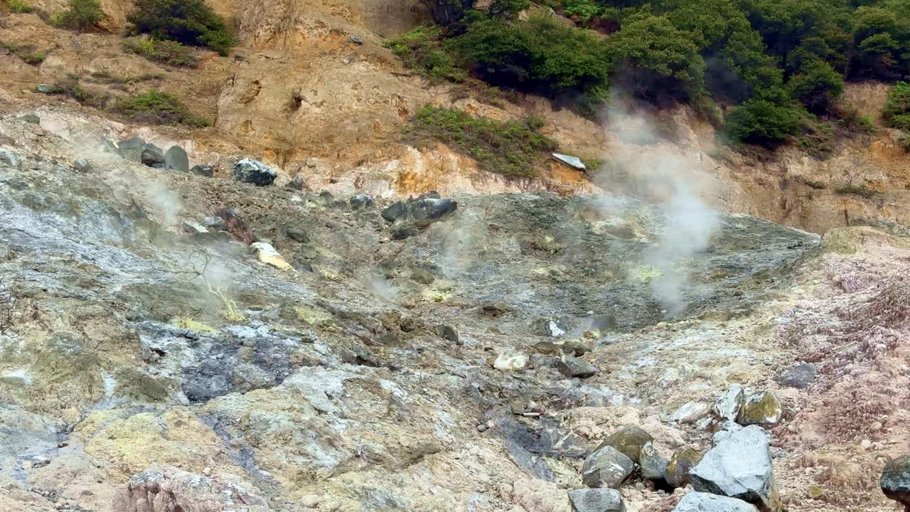 Steam rising from a sulfur-covered rocky slope in a volcanic region, depicting natural geothermal phenomena