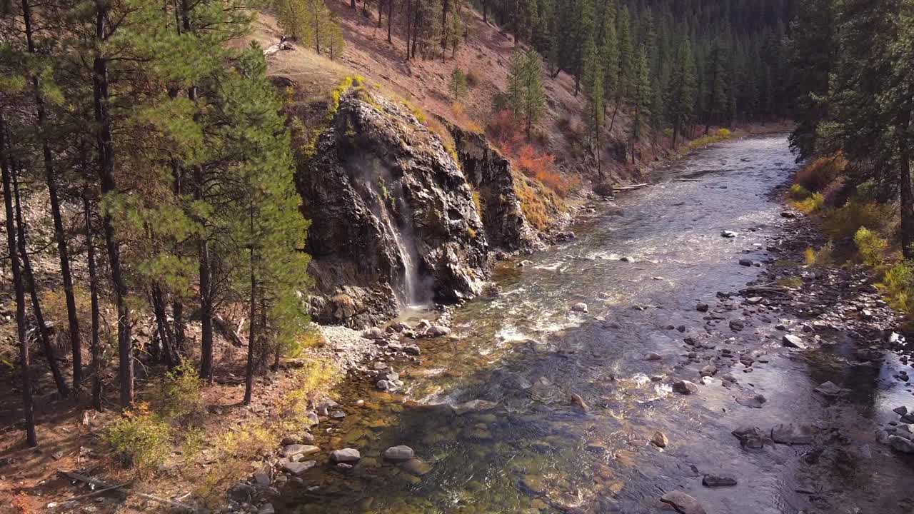 disparo aéreo de drones volando desde río arriba hacia una fuente termal de cascada en el bosque nacional de boise, idaho, con un hermoso río boise que fluye debajo