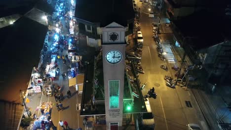 Imágenes-Aéreas-De-La-Torre-Del-Reloj-Conmemorativa-Vietnamita-En-La-Provincia-De-Nakhon-Phanom,-Tailandia,-Rodeada-De-Una-Animada-Calle-Peatonal-Nocturna