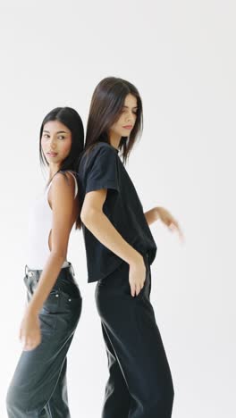 Two women in studio portraits wearing black and white tops and black pants