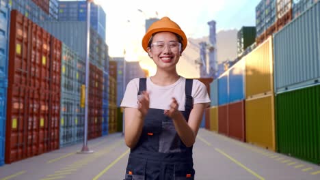 Asian Woman Worker Wearing Goggles And Safety Helmet Smiling And Clapping Her Hands While Standing At Container Yard Warehouse