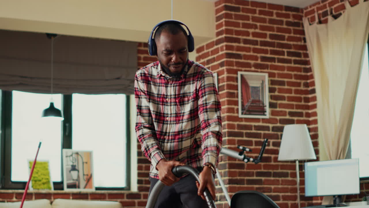African american man using vacuum cleaner to clean wooden floors