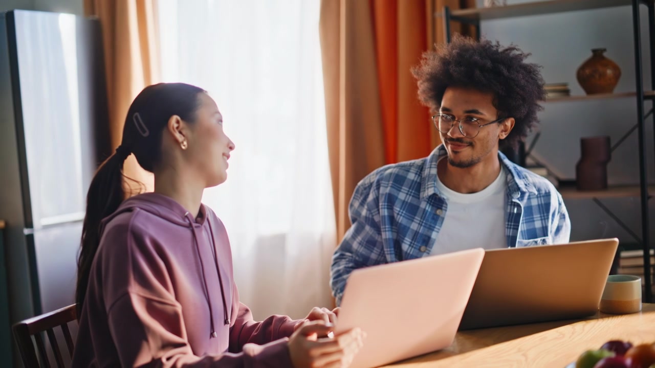 Couple working on laptops in home kitchen. Closeup of freelancers discussing