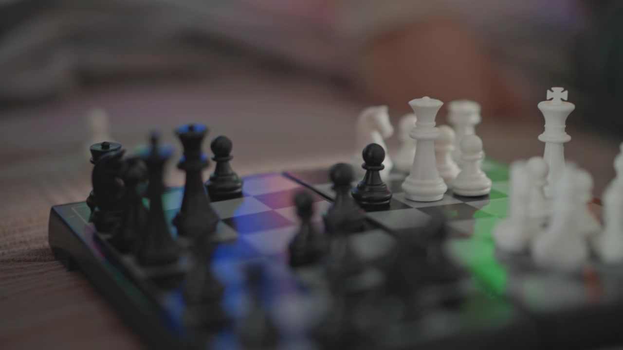 Detalhe em close-up em ângulo baixo de um tabuleiro de xadrez de viagem portátil com peças pretas avançando em direção ao centro enquanto as peças brancas permanecem agrupadas por perto, sugerindo jogo ativo, posicionamento cuidadoso e movimento.