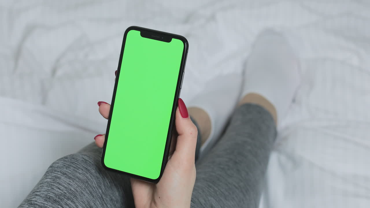 Woman holding a phone with a green screen on a bed