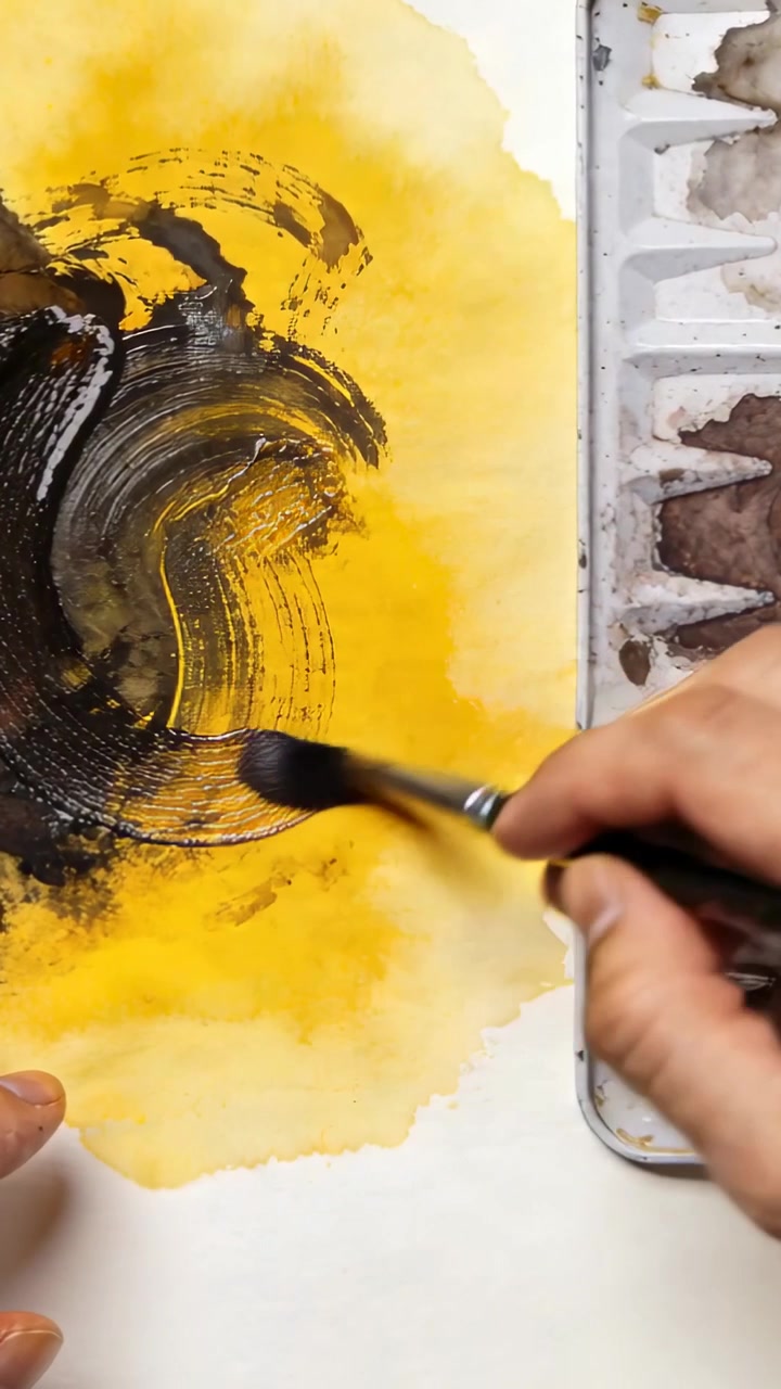 Video verticale: Artista che intinge il pennello nella tavolozza, creando un cerchio su una campitura gialla alla scrivania, con spazio per il testo.