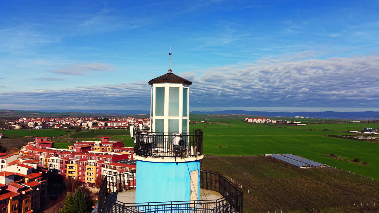 Nahe Luftaufnahme eines Leuchtturm-Laternenraums und Balkons, mit einer Stadt und grünen Feldern, die im unscharfen Hintergrund sichtbar sind. Oberer Teil eines modernen Leuchtturm-Turms.