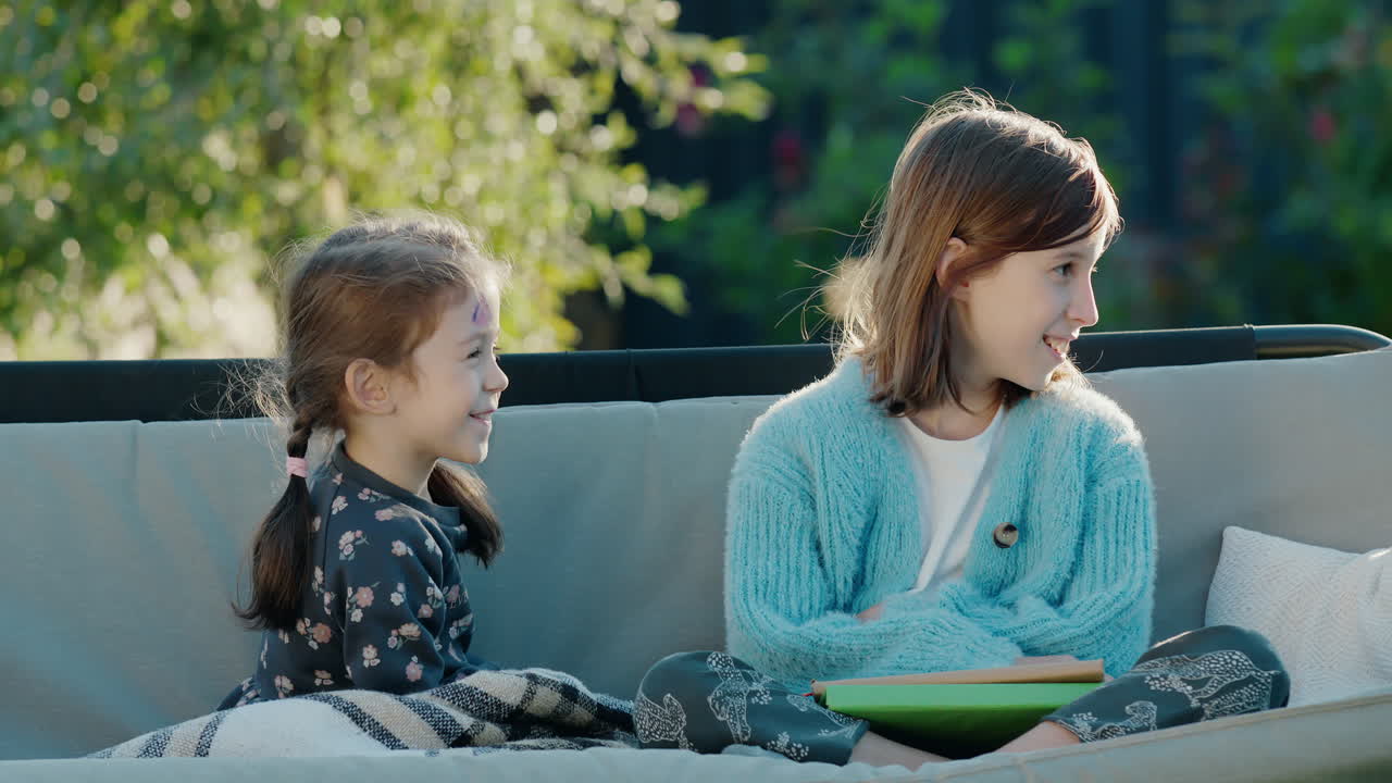 dos hermanas se están relajando en un columpio en el patio trasero de la casa.