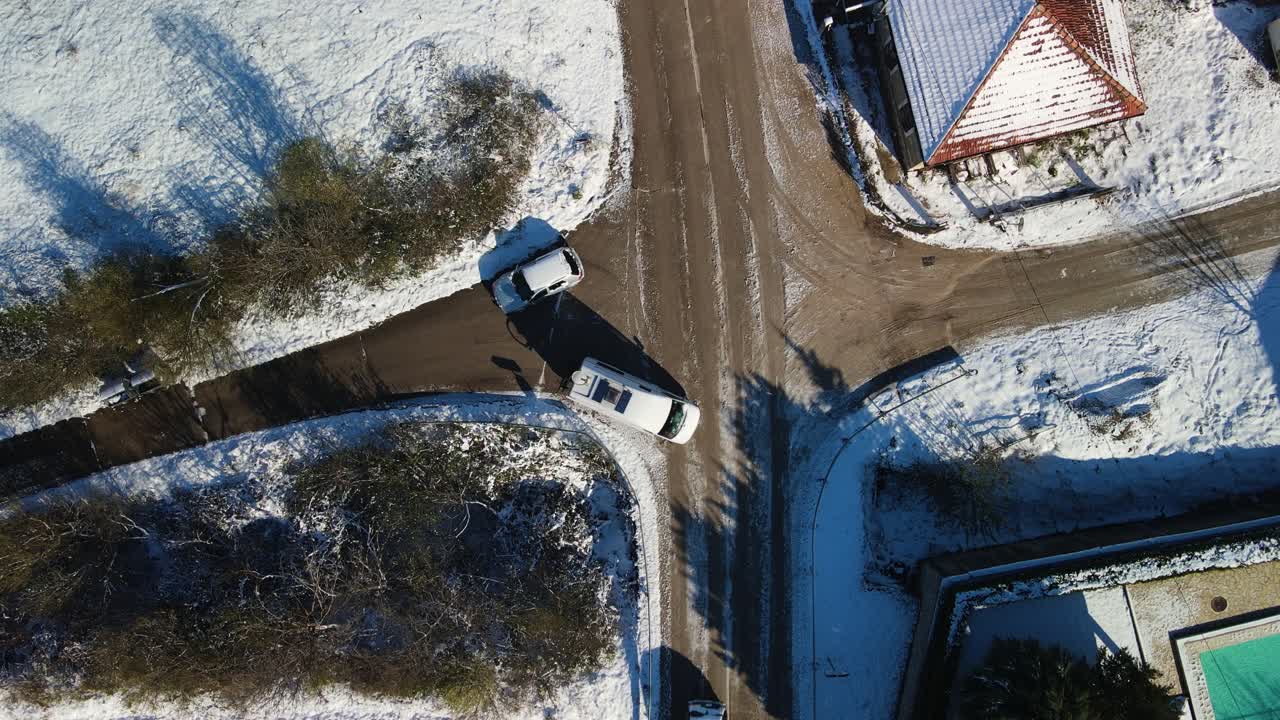 Aerial view several vehicles passing at a crossroad in rural snowy landscape on a sunny winter day, Dalmatia, Croatia