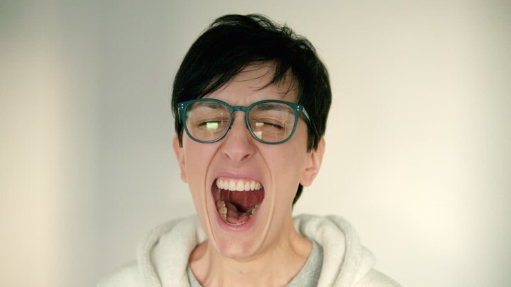 Close up of young woman and with glasses and short hair is tired and yawning
