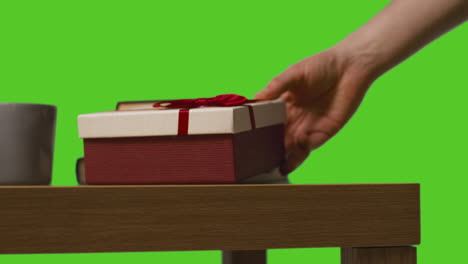 close up of man putting down gift wrapped present onto table shot against green screen