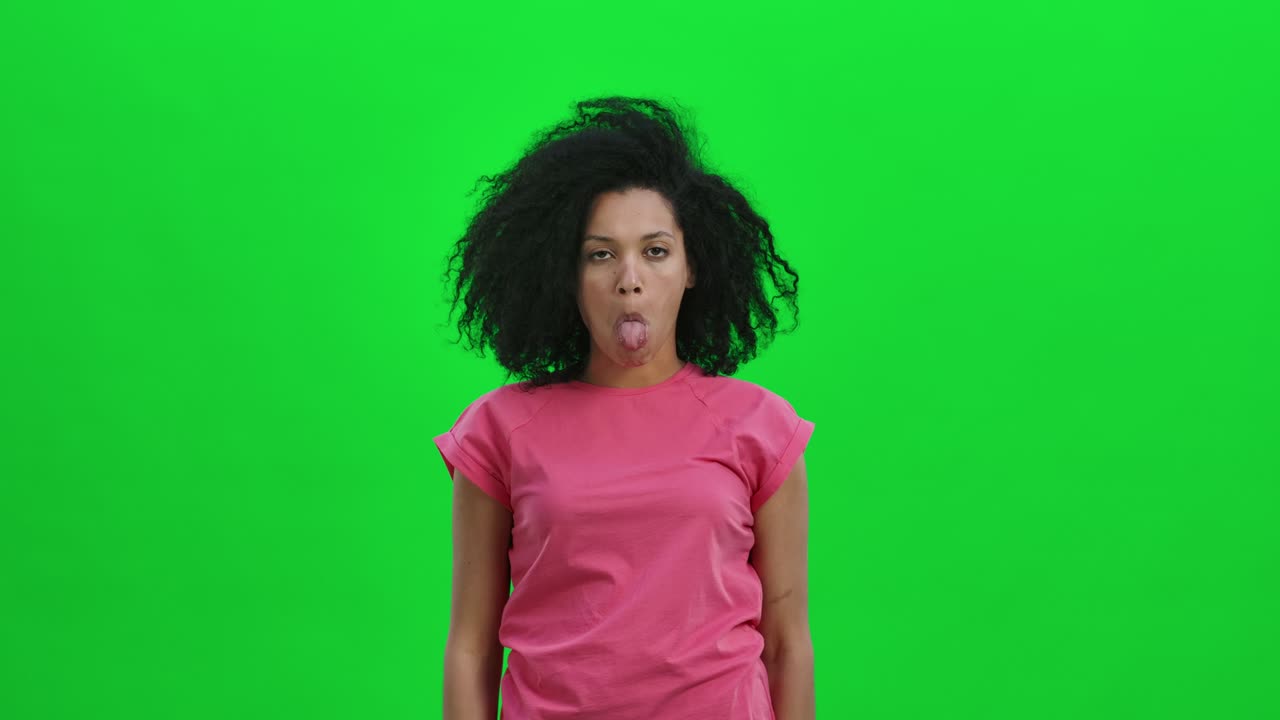 Retrato de jovem mulher afro-americana posando para a câmera fazendo caretas engraçadas. Mulher negra com cabelo cacheado posa em tela verde no estúdio. Close-up. Pronto para câmera lenta a 59,97fps