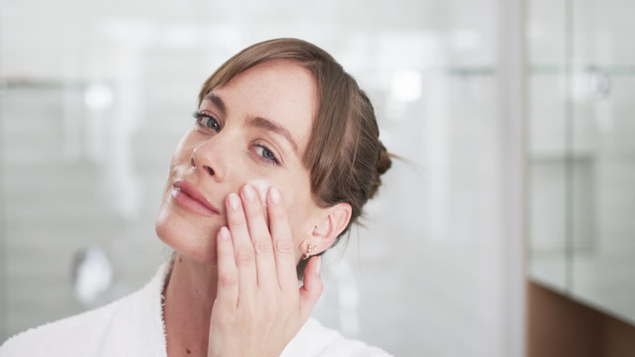mujer caucásica de mediana edad aplica crema facial en casa, con espacio para copiar