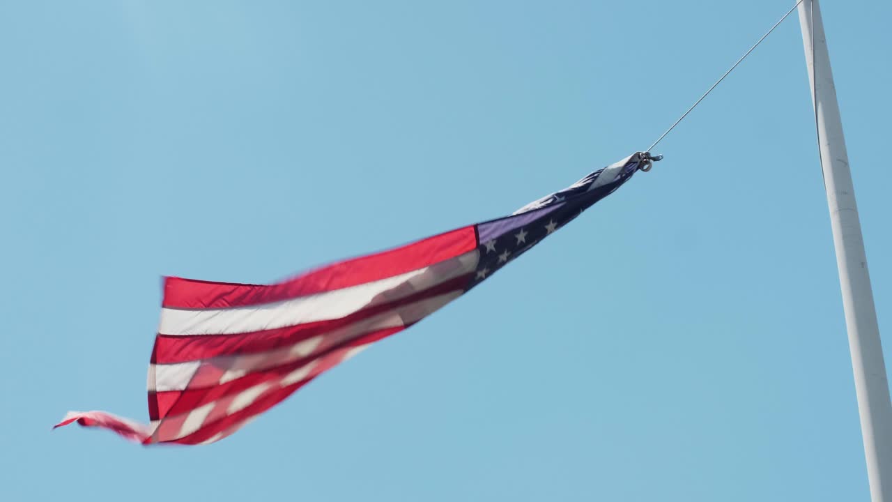Handheld shot of a US flag on a pole hanging on one string on a windy day with clear blue skies