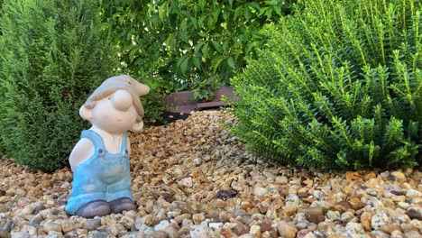 a cute garden gnome in work overalls standing in a flower bed, decorative stones, plants