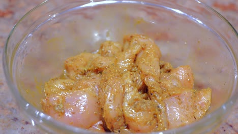 primer plano de pollo marinado con varias especias en un recipiente de vidrio sobre una mesa de mármol