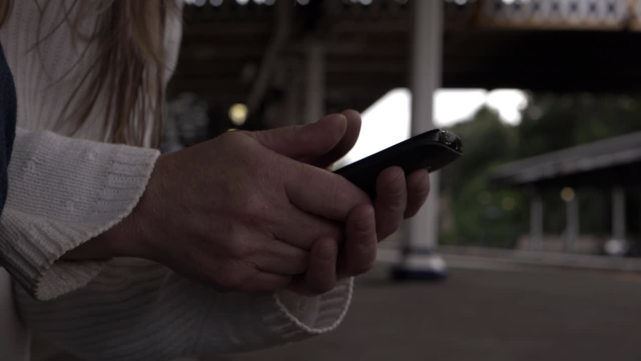 Donna che guarda il cellulare sul binario del treno, inquadratura media