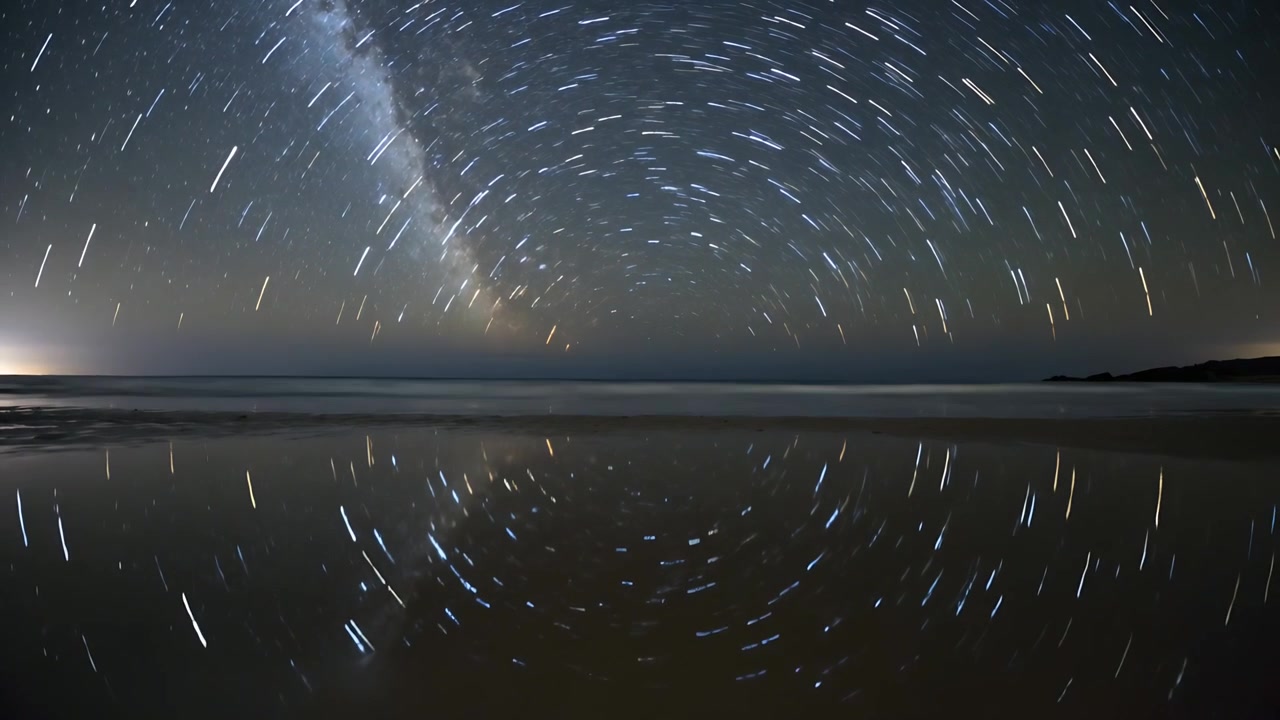 Kamera time-lapse dengan pewaktu merekam jejak bintang berputar yang terpantul di pantai pada malam hari, Bima Sakti.