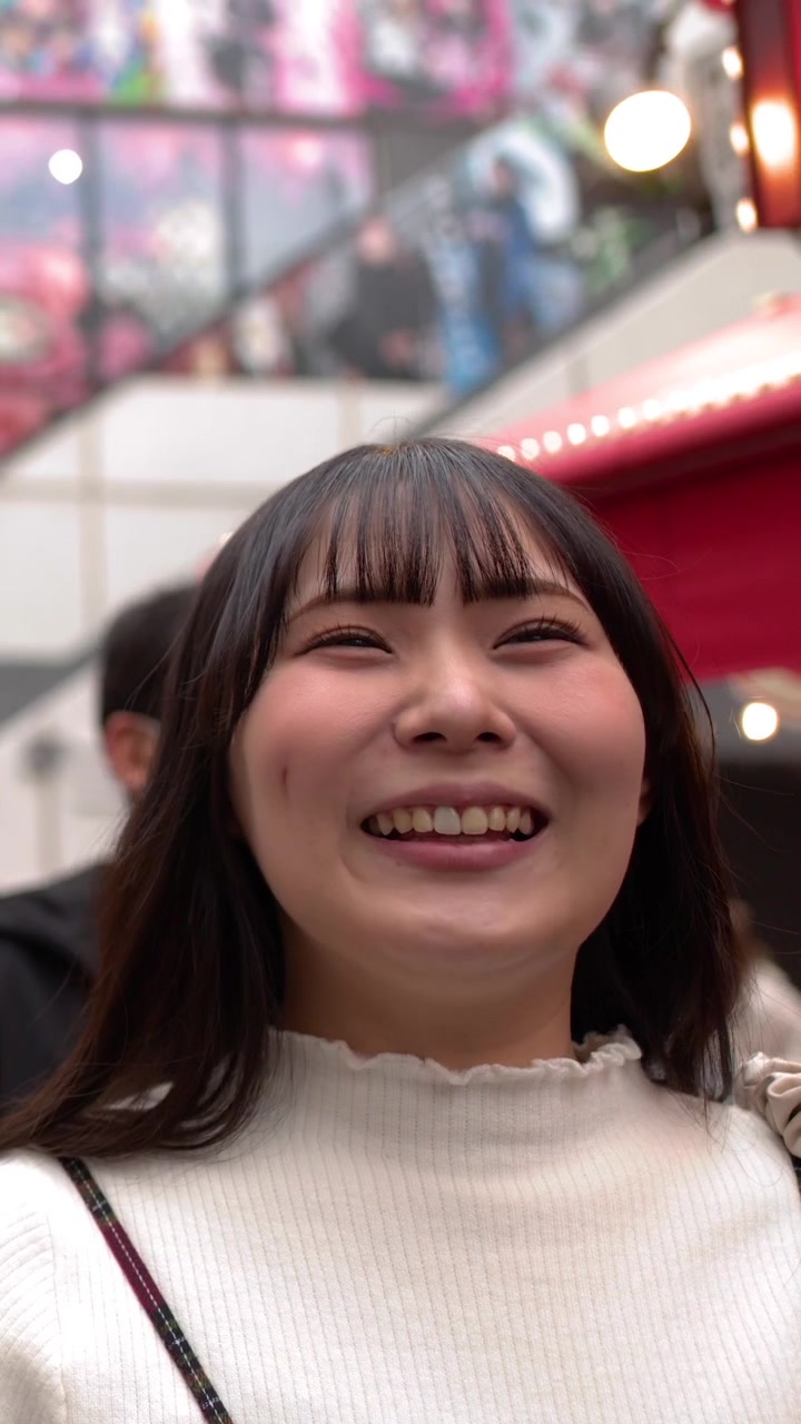Seorang wanita muda yang ceria tersenyum dan tertawa saat berdiri di distrik perbelanjaan Tokyo yang ramai