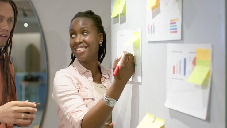 African American team showing charts on office wall, marking with red pen, reviewing data on tablet