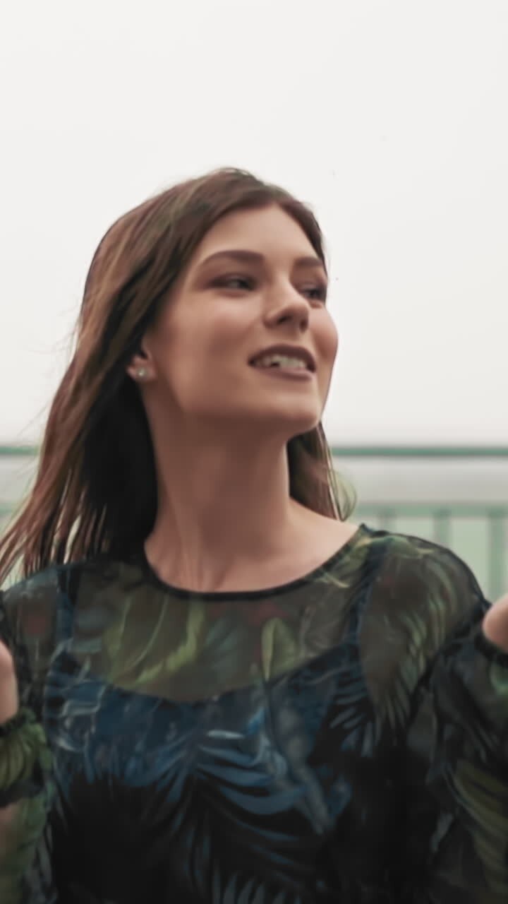 Pretty long haired woman wearing elegant dress looks at cloudy sky waiting for rain beginning on viewpoint against blurry city close view slow motion