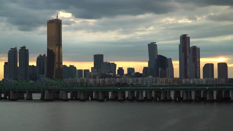 63-Quadratische-Wolkenkratzer-Und-Hochhäuser-Auf-Der-Insel-Youido-Bei-Sonnenuntergang---Zug,-Der-Den-Han-fluss-Durch-Die-Hangang-eisenbahnbrücke-In-Korea-überquert