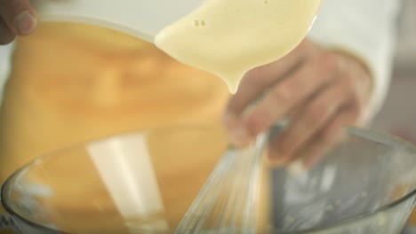 Chef-puts-some-egg-yolk-cream-with-a-plastic-spoon-out-of-a-glass-bowl-and-holds-it-up