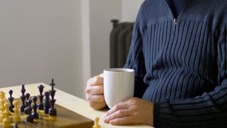 Mann-Trinkt-Kaffee,-Während-Er-Im-Wohnzimmer-Schach-Spielt