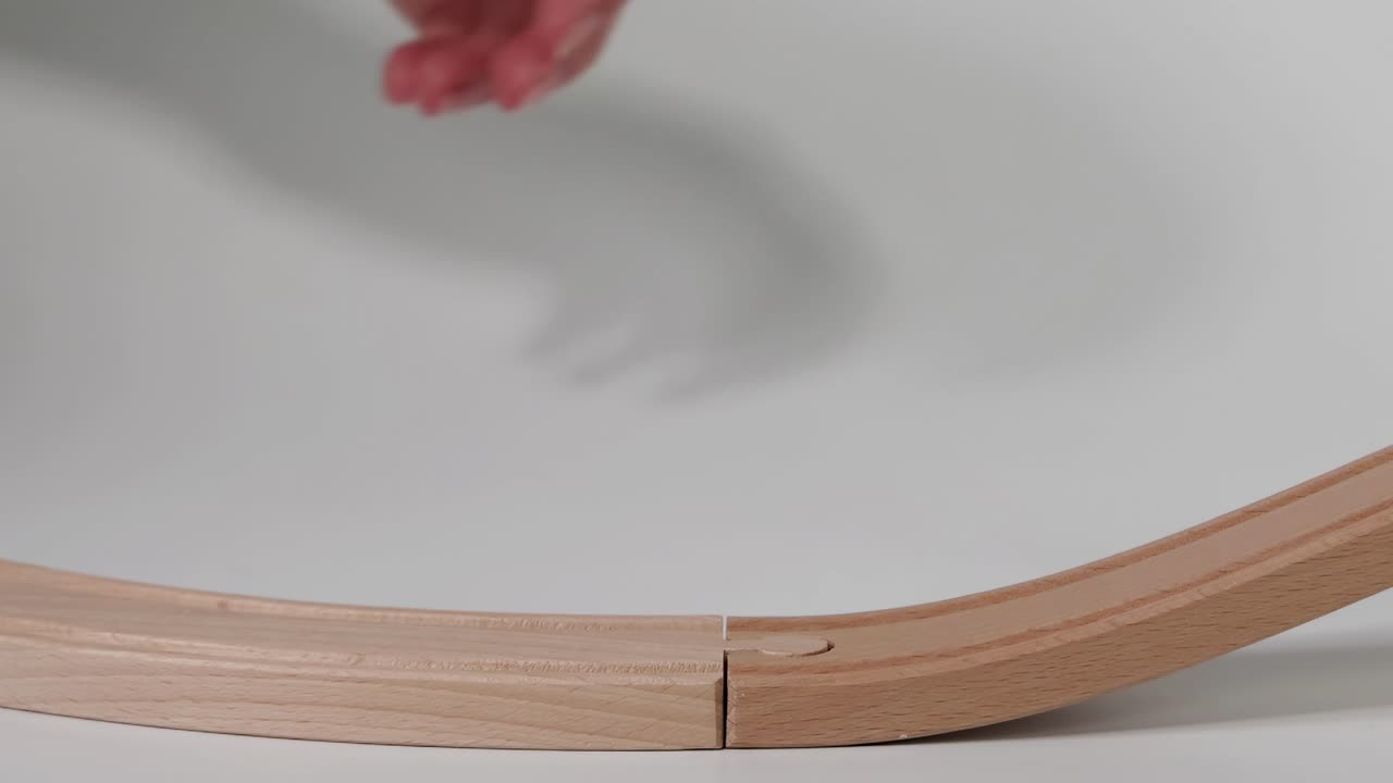 A hand guides a small toy car along a curved wooden track, demonstrating simple motion and play.