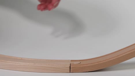 a hand guides a small toy car along a curved wooden track, demonstrating simple motion and play.
