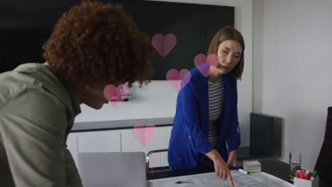 animation of hearts falling over diverse women using laptop