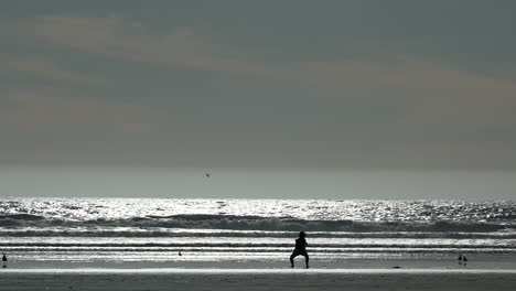 Silhouette-of-a-person-stretching-and-exercising-on-the-beach-at-sunrise-or-sunset