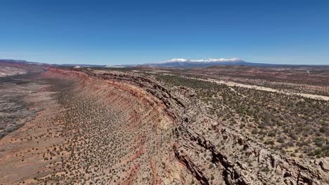 aerial view of steep ridge in desert, rocky jagged edges, snowcapped mountains, northern comb ridge in southeast utah