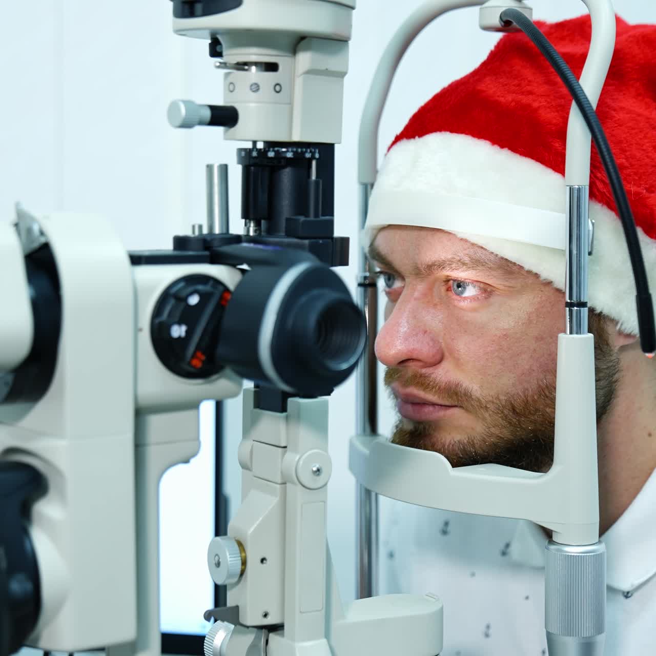 Patient in Christmas cap at ophthalmologist's. Man testing his eyes in clinic. Young male patient checking his eyesight