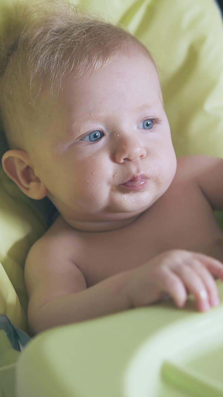 young mommy feeds cute little boy with fresh soup puree in comfortable highchair in light room closeup