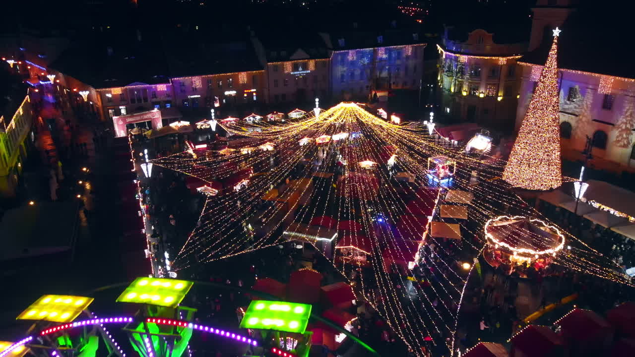 Aerial drone view of The Big Square in Sibiu at night, Romania. Old city centre decorated for Christmas. Ferris wheel, skating rink, people