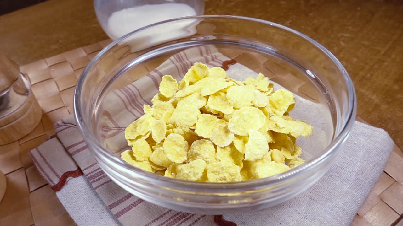 Knusprige gelbe Cornflakes in die Schale für ein köstliches Frühstück mit Milch am Morgen. Zeitlupe mit rotierender Kamerafahrt