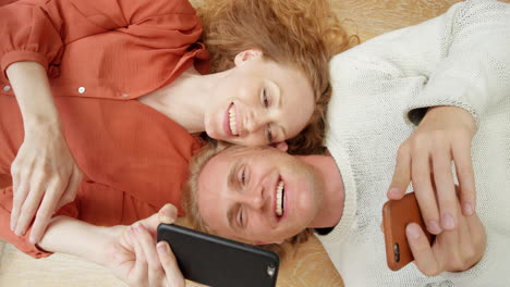 couple laying on the floor, sharing a moment on their phones
